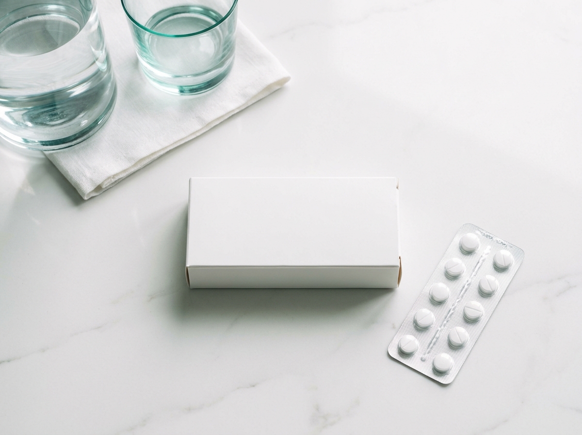 Plaquette de comprimés génériques blancs, boîte cartonnée pharmaceutique blanche et carafe d'eau posées sur un plan en marbre clair
